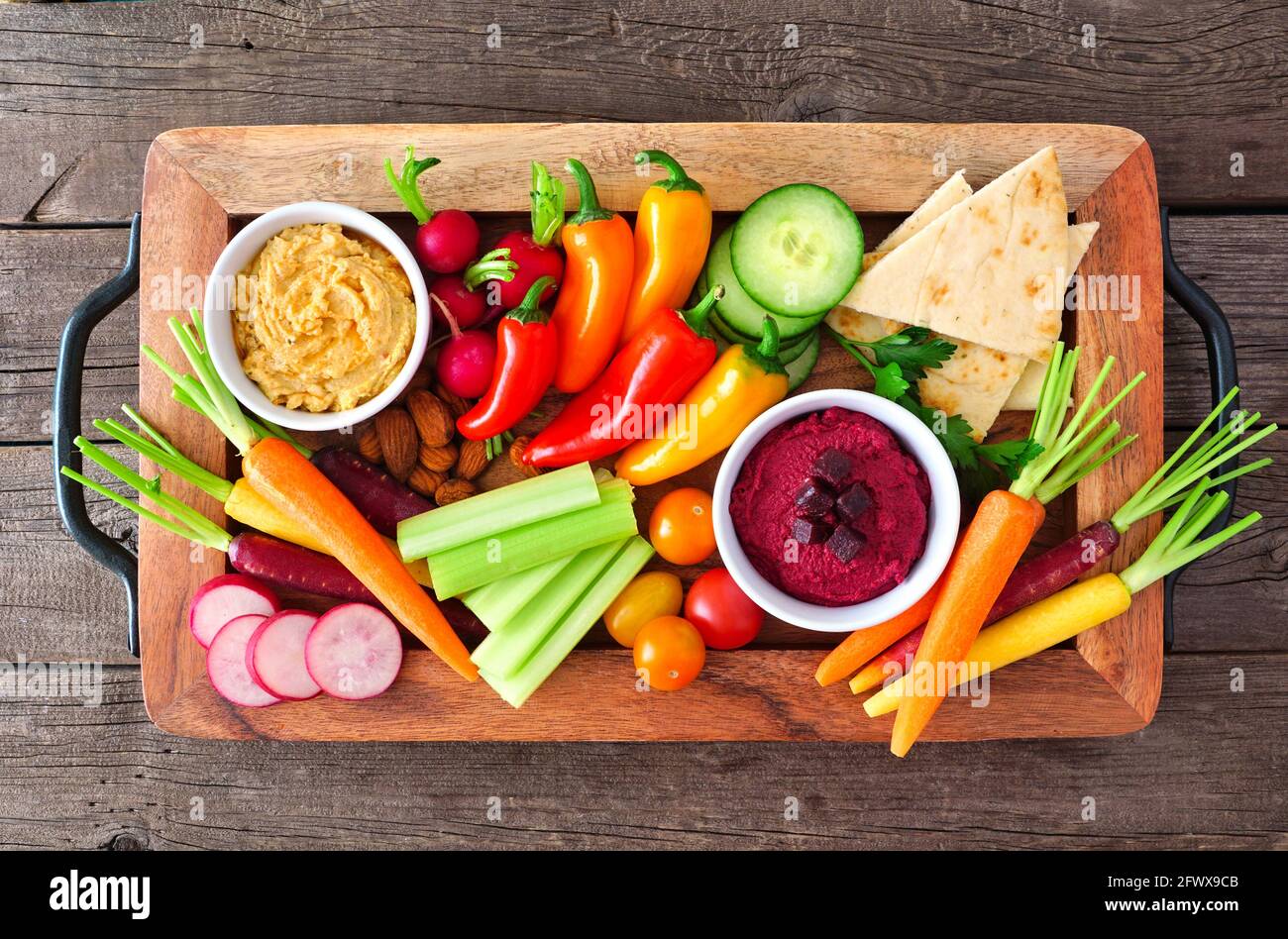 La varietà di verdure fresche e l'hummus si tuffano su un vassoio da portata sopra la vista su uno sfondo rustico di legno. Foto Stock