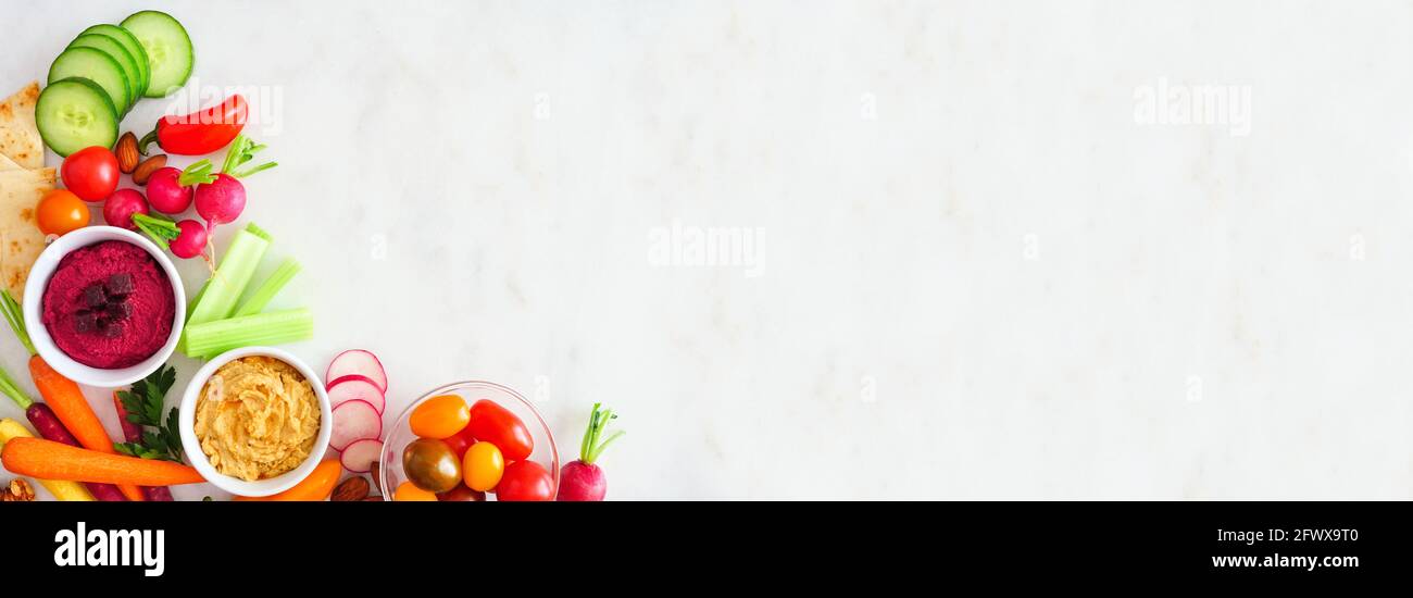 Verdure fresche miste e hummus. Bordo dell'angolo della vista dall'alto su uno sfondo di marmo bianco. Foto Stock