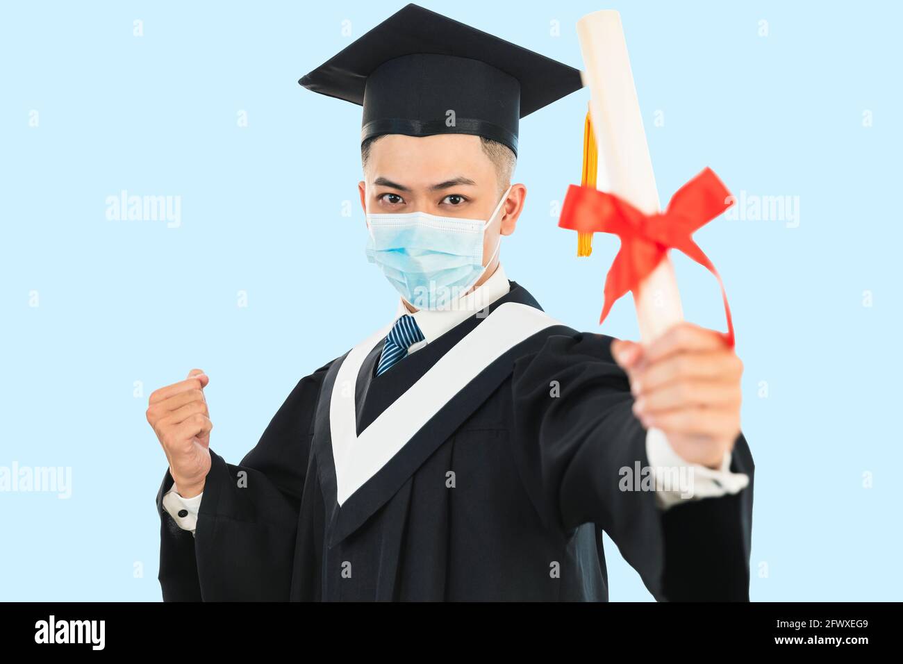 giovane laurea maschile indossando maschera facciale e tenendo il suo collegio certificato durante la pandemia del coronavirus Foto Stock