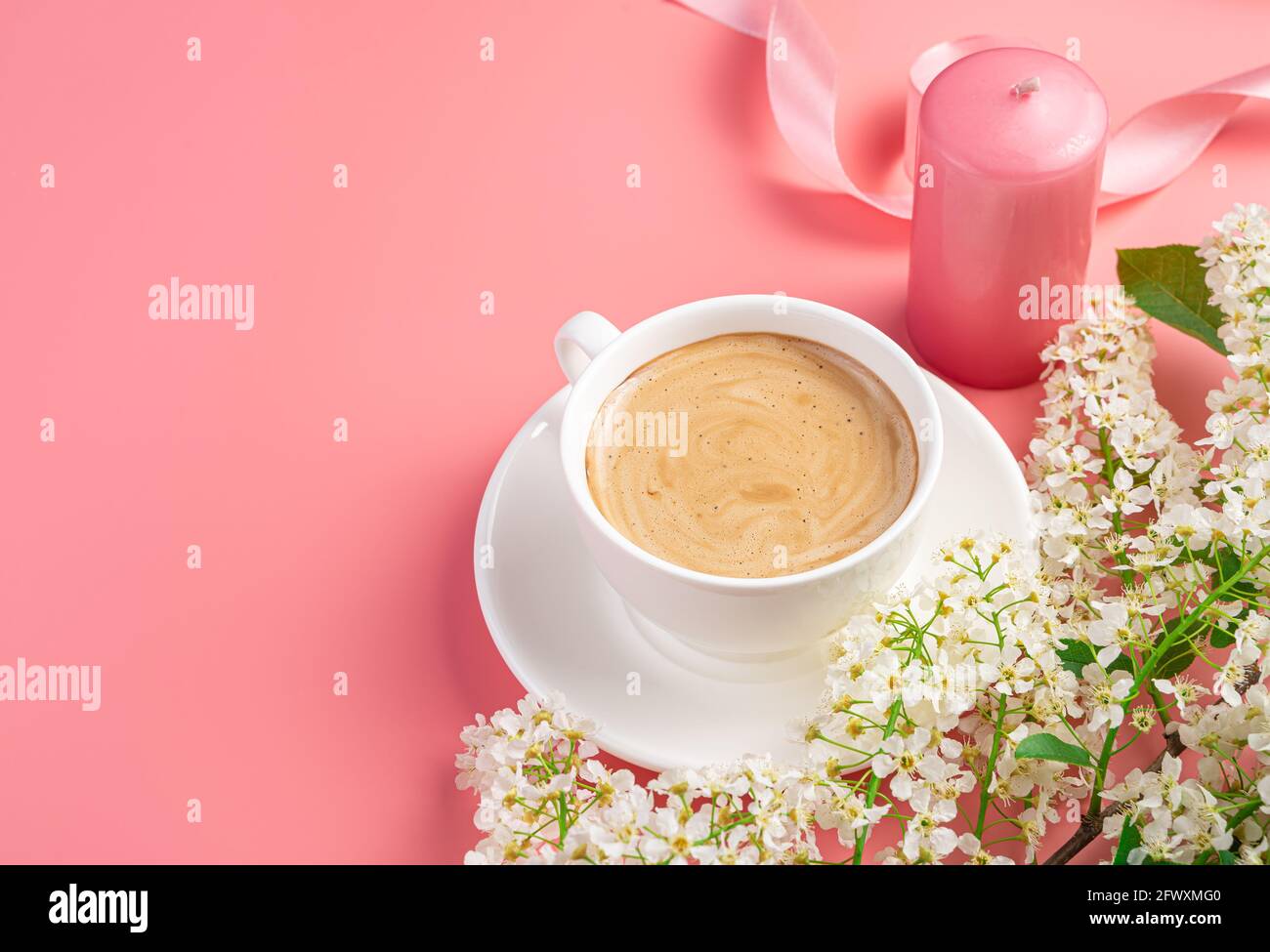 Caffè in una tazza bianca, candela e fiori su uno sfondo rosa con spazio per copiare. Foto Stock