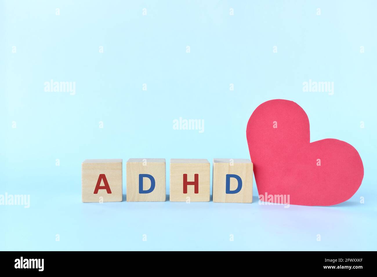 Amare e sostenere i bambini con ADHD o concetto di disturbo da deficit di attenzione iperattività. Lettere ADHD su blocchi di legno accanto a una forma a cuore rosso Foto Stock