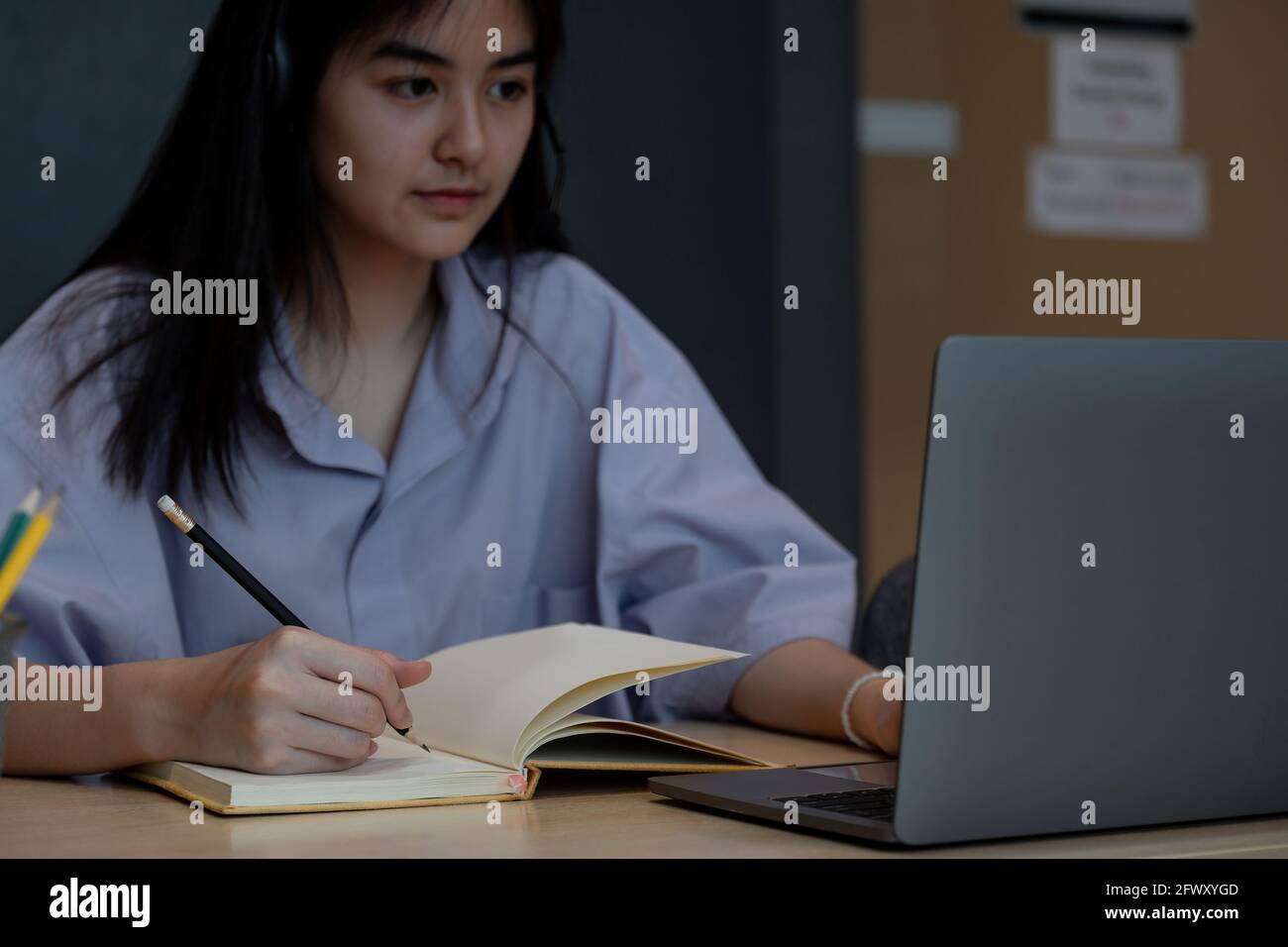 Primo piano di uno studente asiatico che prende nota durante la lezione online con il laptop, Study Education a casa. Foto Stock
