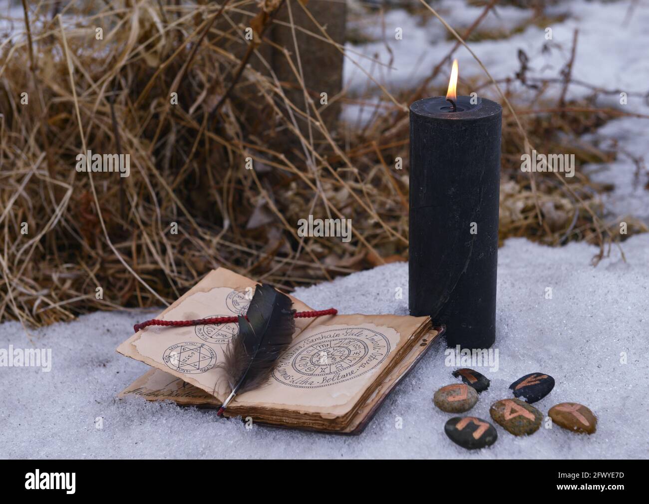 Rituale magico con candela nera, rune su pietre e aperto con libro con  incantesimi sulla neve. Sfondo esoterico, gotico e occulto, mistico di  Halloween e W Foto stock - Alamy