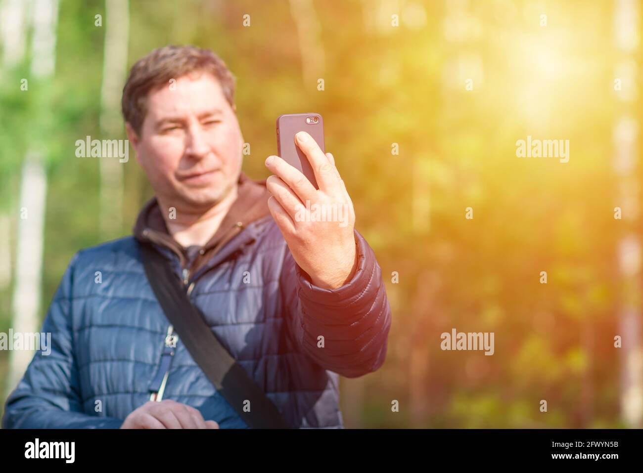 Un uomo di 40 anni con il suo smartphone cellulare alla ricerca del segnale di ricezione nella foresta primaverile soleggiata. Foto Stock