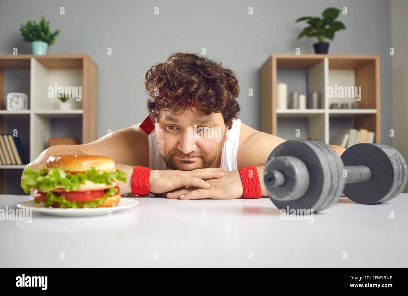 Divertente triste uomo chubby scelta tra palestra dumbbell e delizioso hamburger malsano Foto Stock