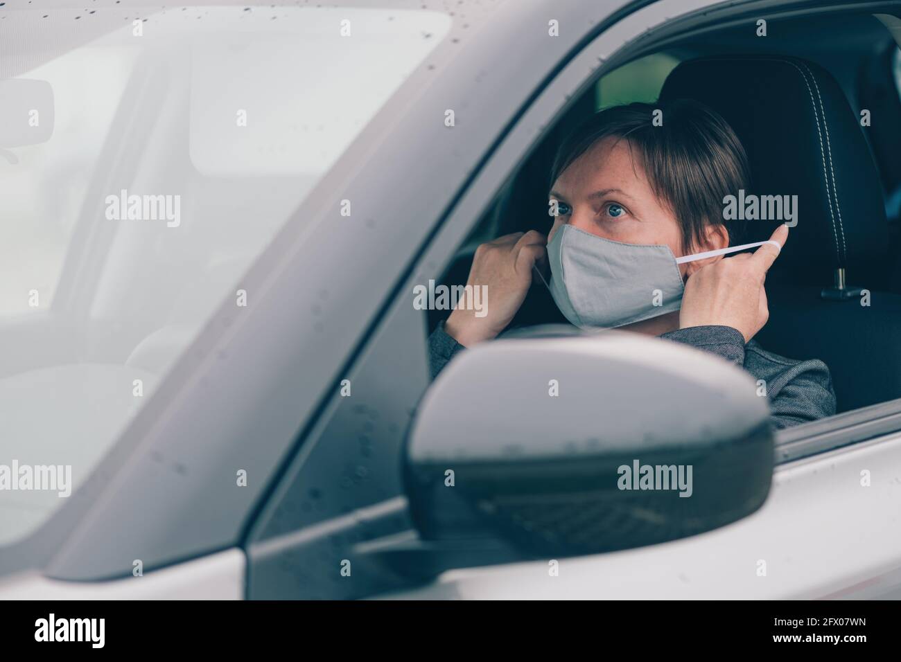 Donna che indossa una maschera protettiva in auto durante le pandemie covid-19, guardando lo specchio, fuoco selettivo Foto Stock