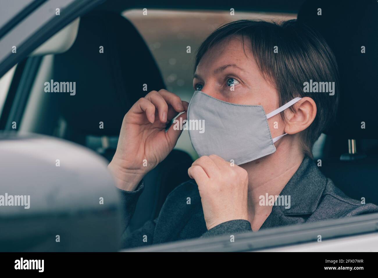 Donna che indossa una maschera protettiva in auto durante le pandemie covid-19, guardando lo specchio, fuoco selettivo Foto Stock