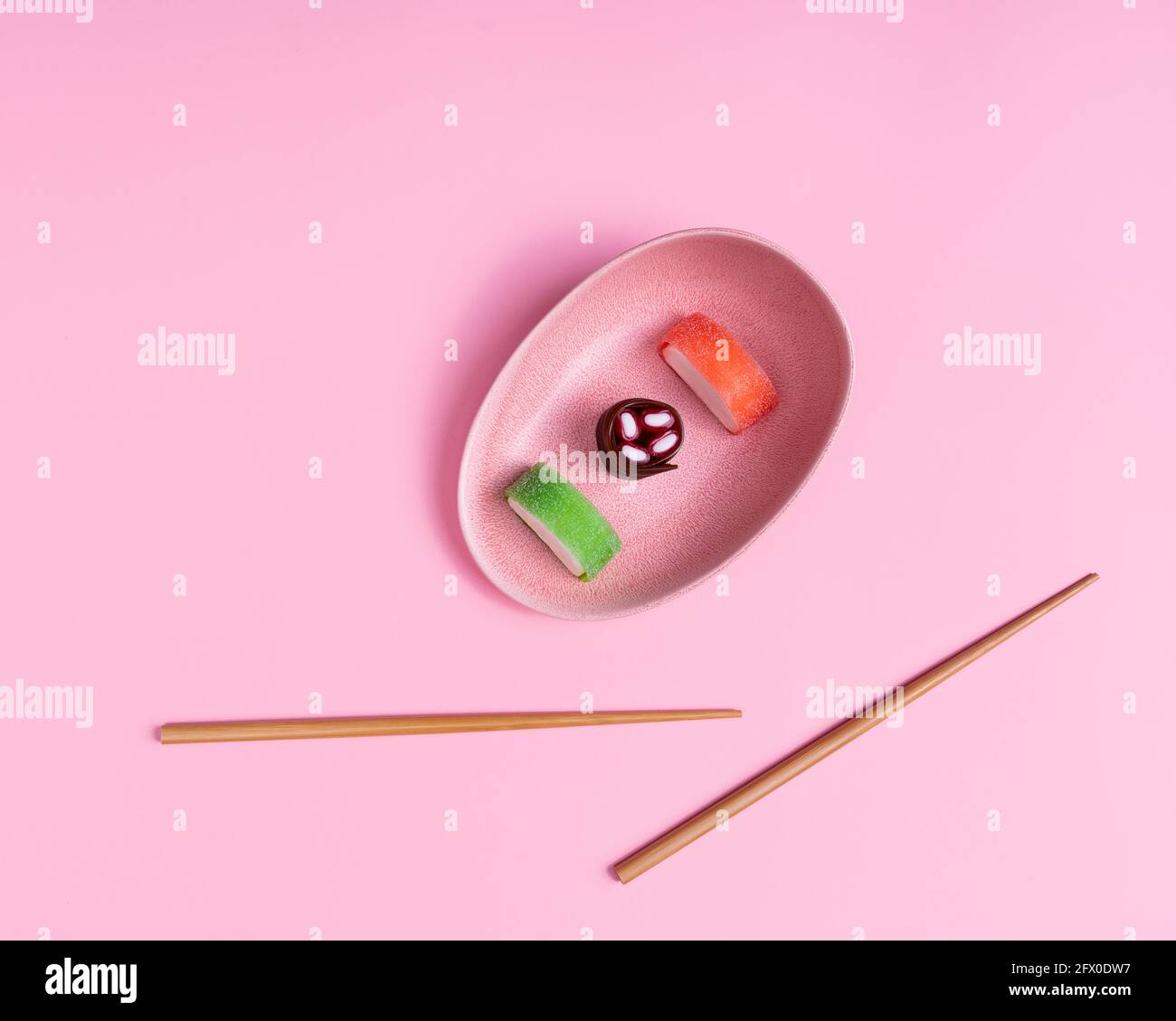Vista dall'alto di appetitosi sushi dolci colorati serviti su ceramica piatto con bastoncini di legno posti su sfondo rosa Foto Stock