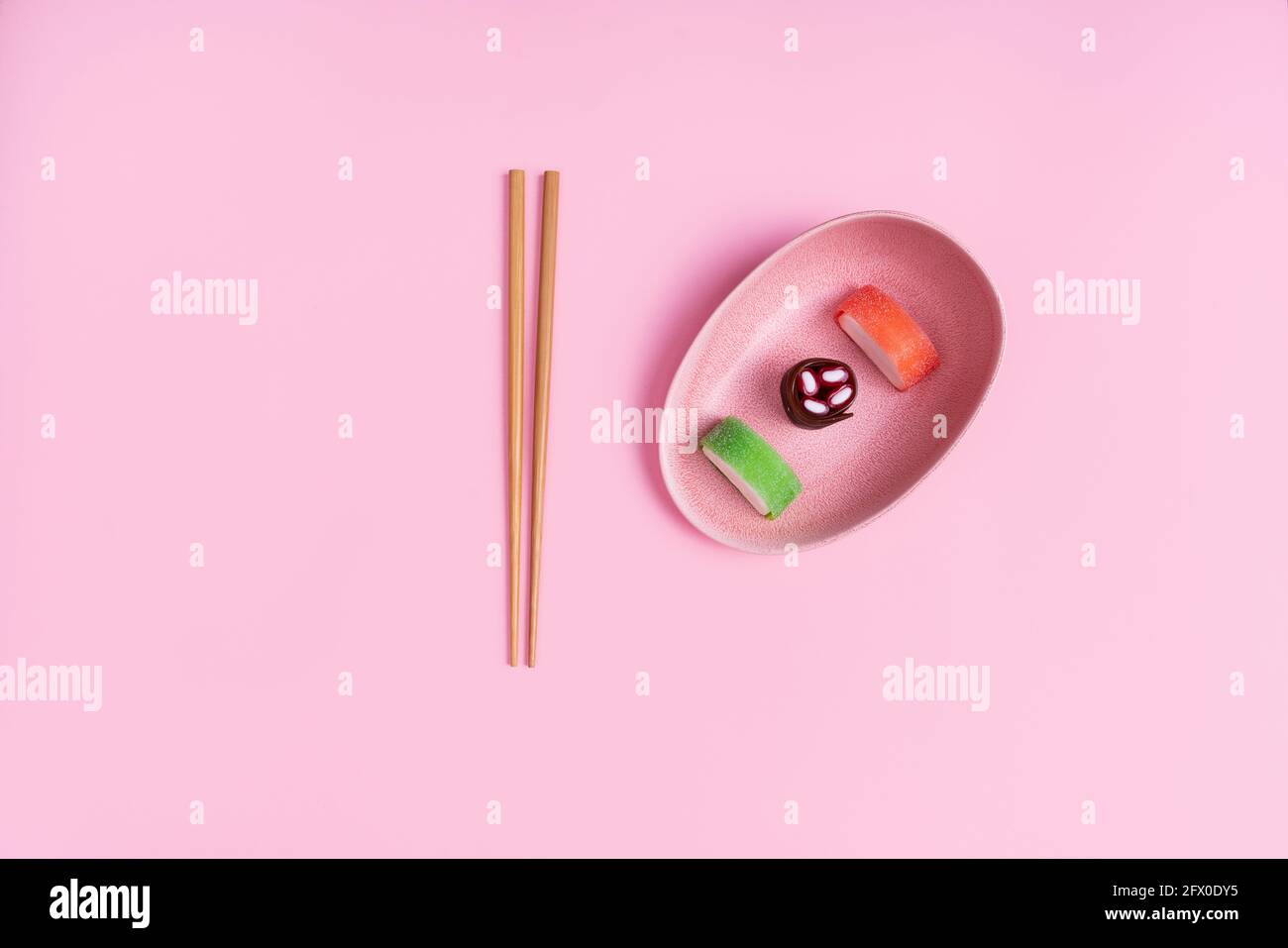 Vista dall'alto di appetitosi sushi dolci colorati serviti su ceramica piatto con bastoncini di legno posti su sfondo rosa Foto Stock
