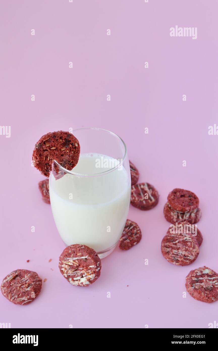Biscotto rosso su un bicchiere di latte con molti altri sparsi su sfondo rosa Foto Stock