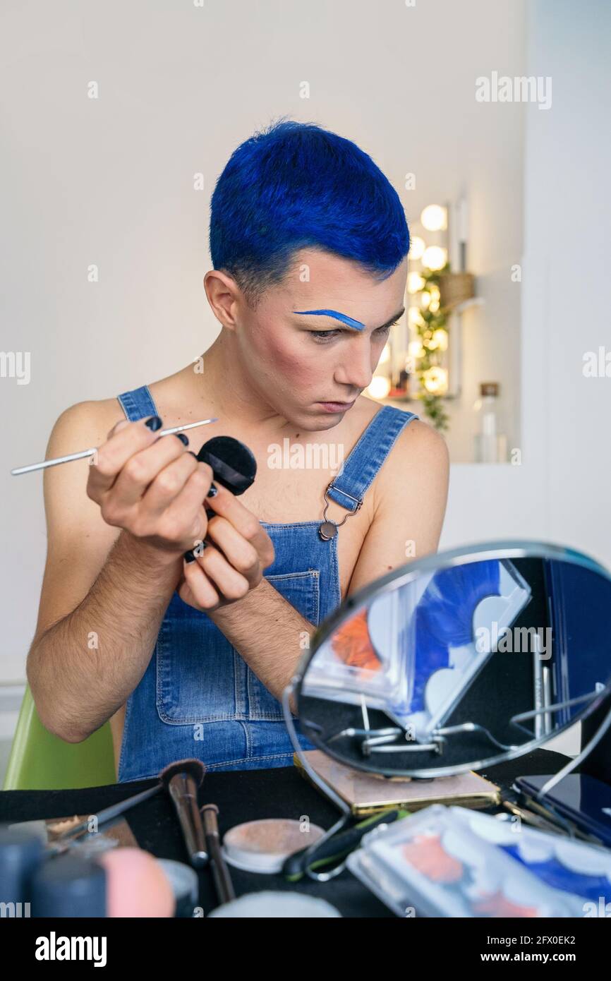 Queer con i capelli blu corti che applicano il trucco e l'aspetto del  trascinamento nello specchio rotondo Foto stock - Alamy