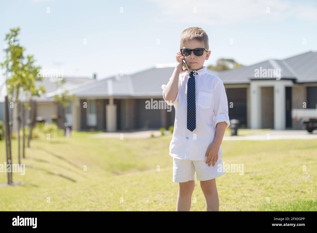 Carino ragazzo australiano che indossa abbigliamento da lavoro con occhiali da sole mentre si utilizza un telefono cellulare in una giornata estiva brillante Foto Stock