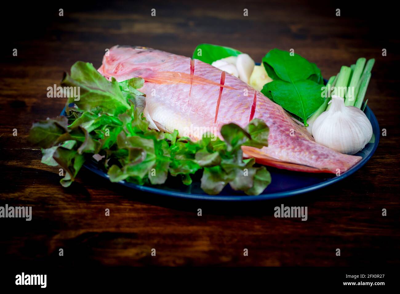 Primo piano un pesce fresco e verdure in piatti di ceramica preparati per la cottura. Foto Stock