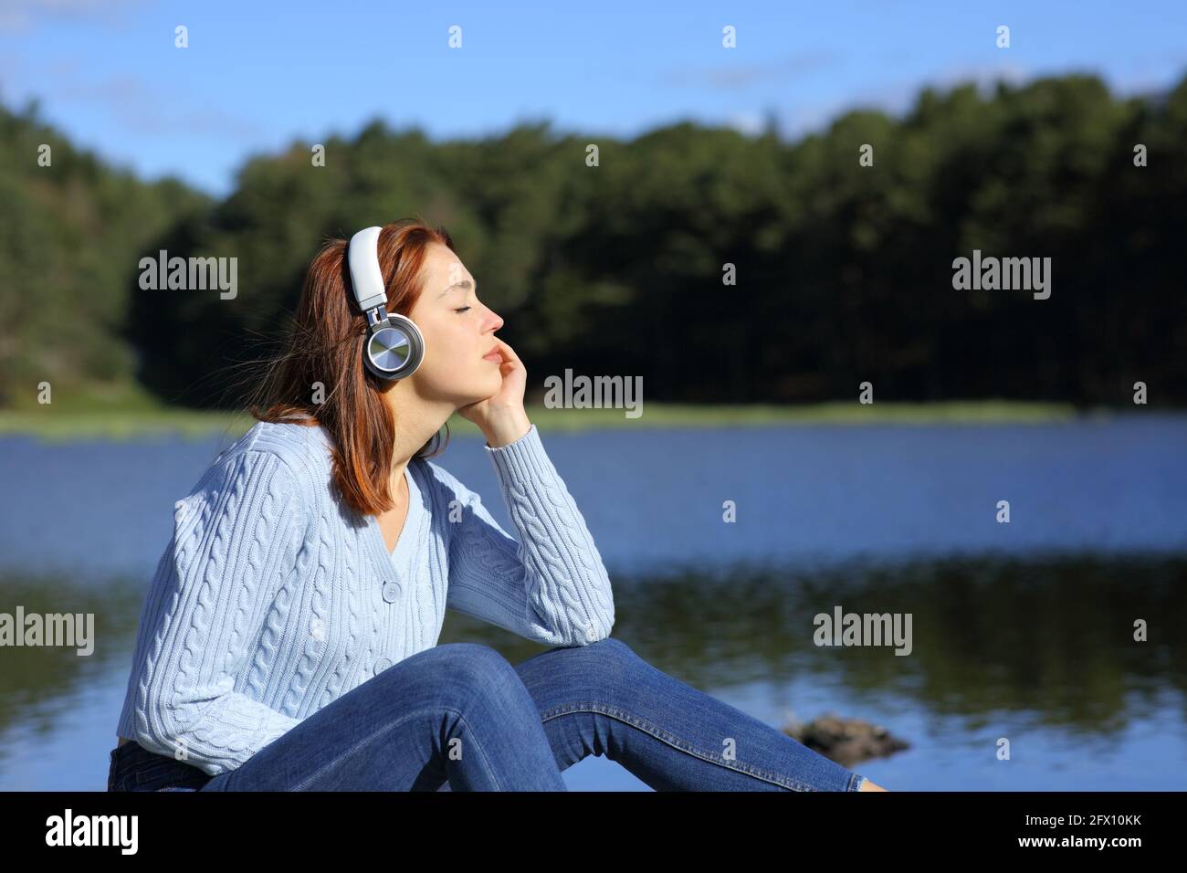 Ritratto in vista laterale di una donna rilassata che ascolta la musica con cuffie wireless in una laguna in montagna Foto Stock