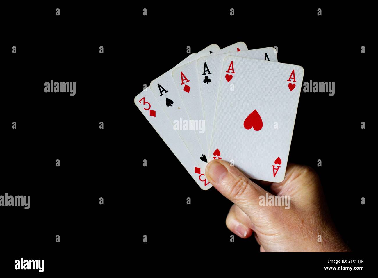 Mano che tiene 5 carte - quattro delle quali sono gli assi. Sfondo nero Foto Stock