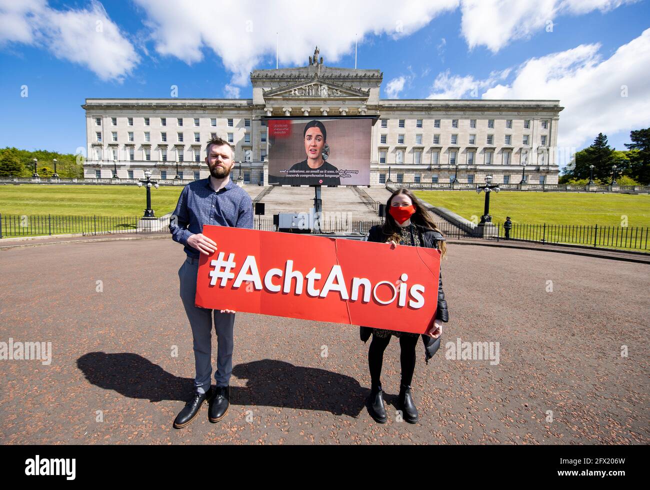 Persone prima del profitto i colleghi Gerry Carroll MLA e Belfast City Assessor Fiona Ferguson stand a Stormont come membri della comunità linguistica irlandese visualizzare uno schermo mobile all'aperto con un messaggio che vede oltre 70 parlanti in lingua irlandese che chiedono l'esecutivo dell'Irlanda del Nord insieme ai governi britannico e irlandese Attuare l'accordo New decade, New Approach (NDNA), una normativa sui diritti linguistici irlandesi, 500 giorni dopo l'accordo. Data immagine: Martedì 25 maggio 2021. Foto Stock