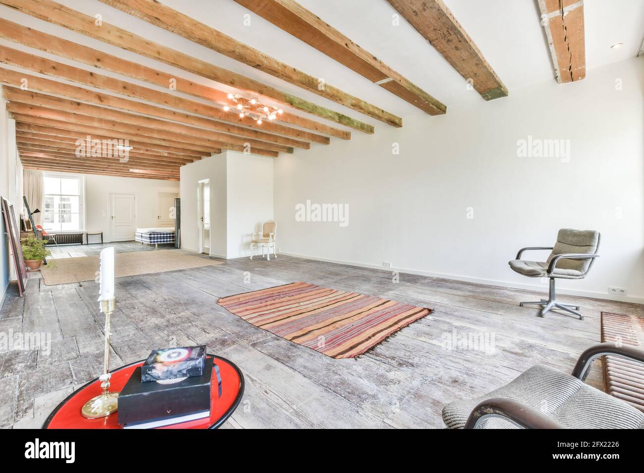 Arredamento minimalista di camera casa luminosa con pavimento in legno con sedie e tappeti sotto il soffitto con travi in legno Foto Stock