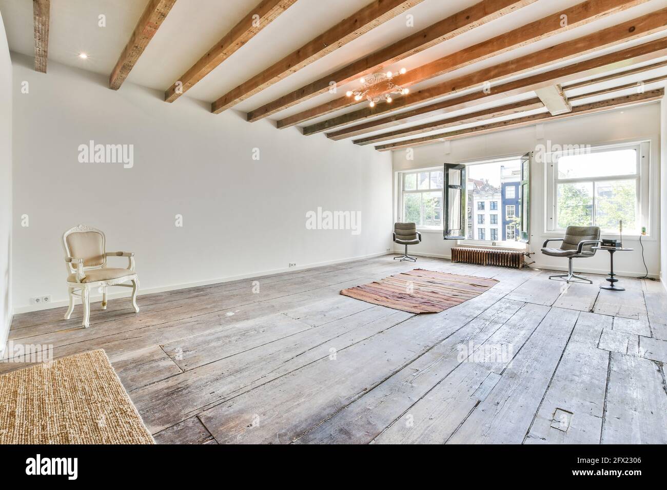Arredamento minimalista di camera casa luminosa con pavimento in legno con sedie e tappeti sotto il soffitto con travi in legno Foto Stock