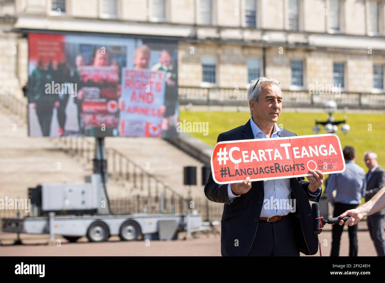 Pat Sheehan MLA per Sinn Fein a Stormont, in quanto membri della comunità linguistica irlandese, presentano uno schermo mobile all'aperto con un messaggio che presenta oltre 70 oratori di lingua irlandese, invitando l'esecutivo dell'Irlanda del Nord e i governi britannico e irlandese ad attuare il nuovo decennio; New Approach (NDNA) Deal, legislazione in materia di diritti linguistici irlandesi, 500 giorni dopo l'accordo. Data immagine: Martedì 25 maggio 2021. Foto Stock