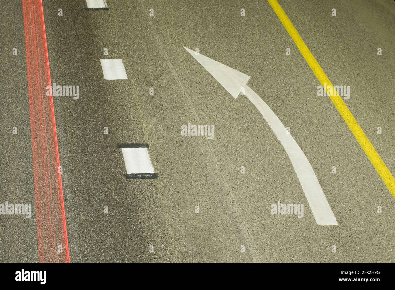 Freccia di svolta a sinistra sulla strada tra continua e discontinua. Sulla sinistra, un pennacchio rosso dalle luci di un'auto che passa. Vista dall'alto Foto Stock