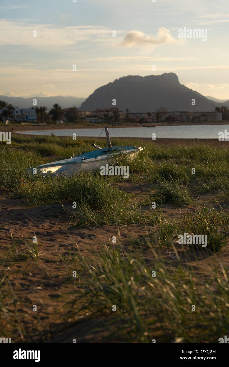 Barca intrecciata in erba su una spiaggia di sabbia. Piccola barca bianca. È circondato da erba nella sabbia. Foto Stock