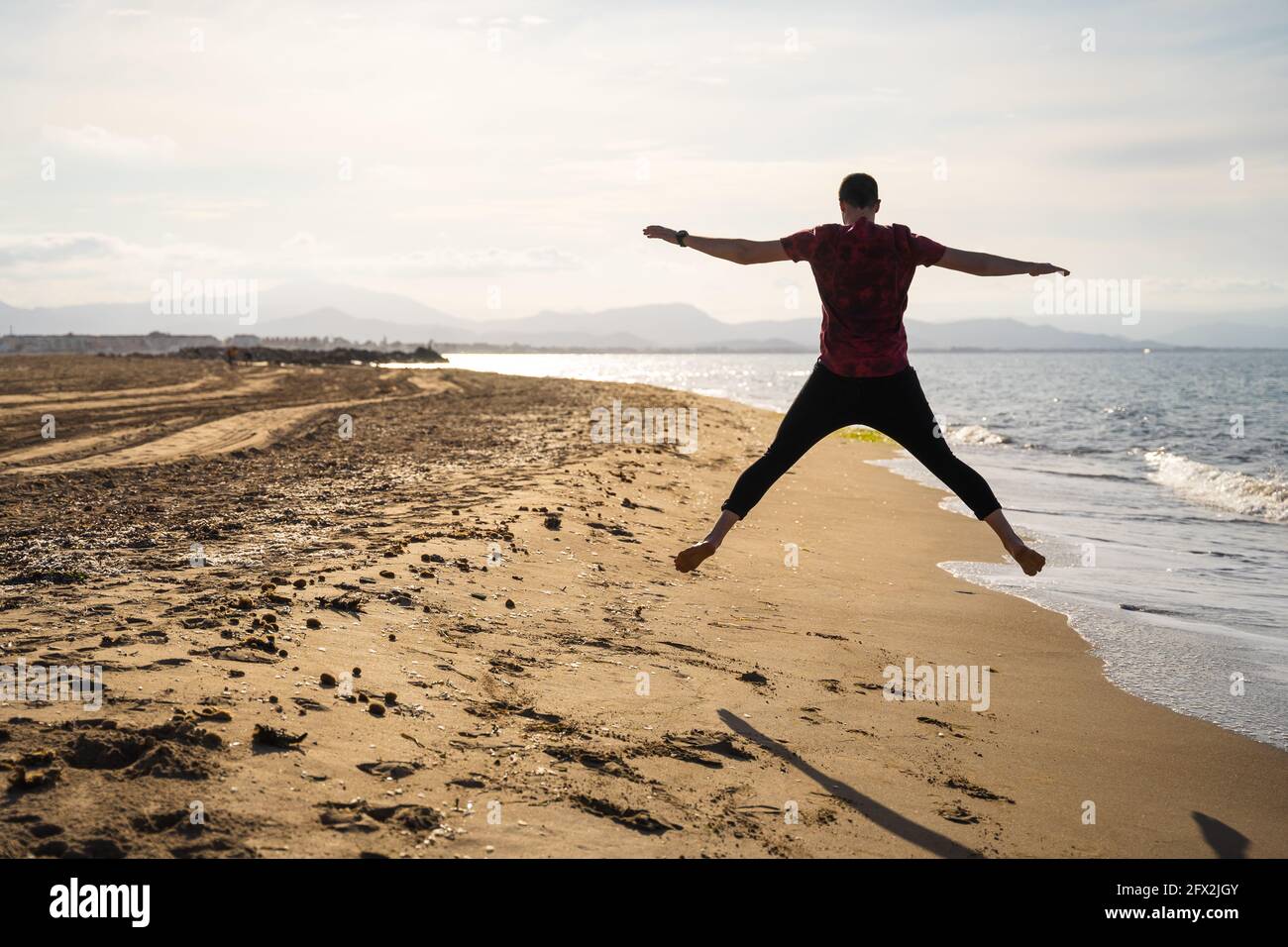 Uomo che salta in riva al mare in una giornata di sole. Caucasica con pantaloni  lunghi e camicia a maniche corte. L'ombra può essere vista sulla sabbia  dorata Foto stock - Alamy