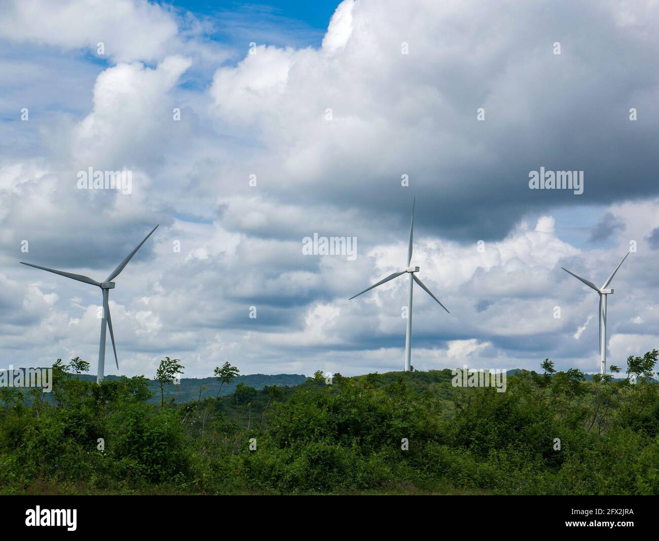 Turbine eoliche sul verde terreno collinare con il cielo blu luminoso. Foto Stock