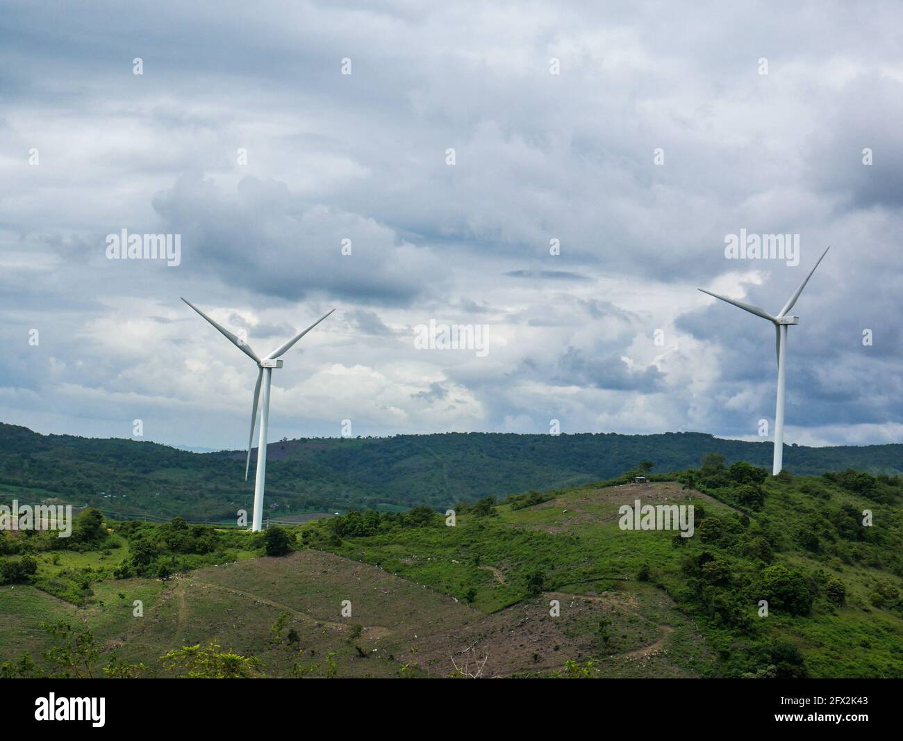Turbine eoliche sul verde terreno collinare con il cielo blu luminoso. Foto Stock