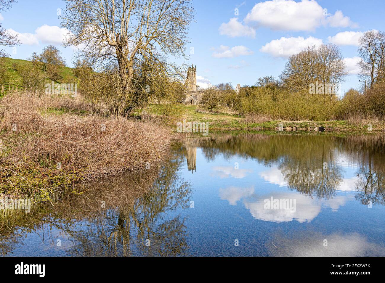 Le rovine della chiesa di St Martins si riflettono in un laghetto di mulini abbandonato a Wharram Percy, nel villaggio medievale desertico sullo Yorkshire Wolds, North Yorkshire. Foto Stock