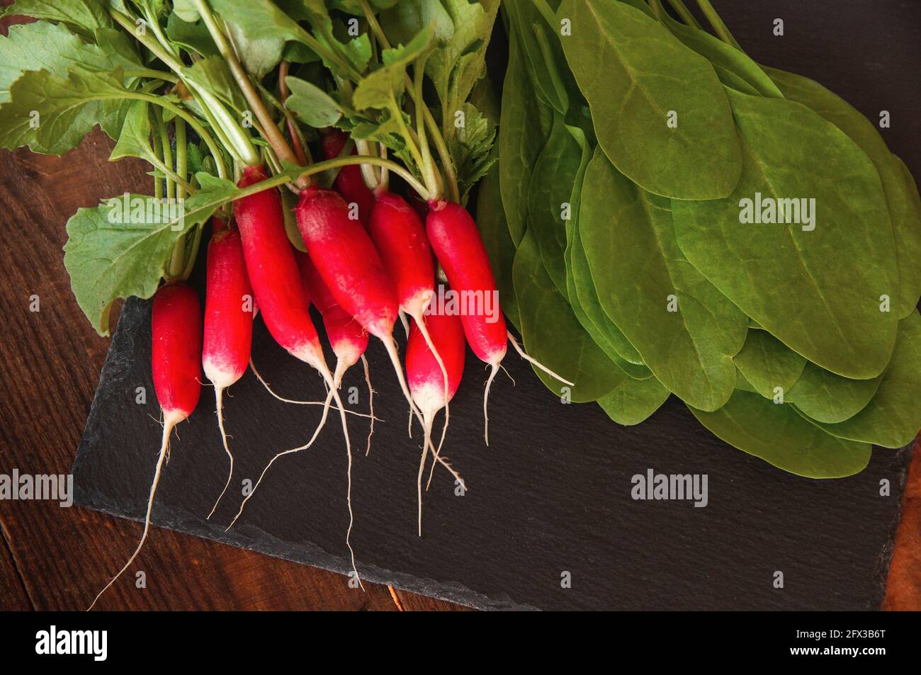 i ravanelli freschi con foglie e spinaci giacciono su un nero tavola di servizio Foto Stock
