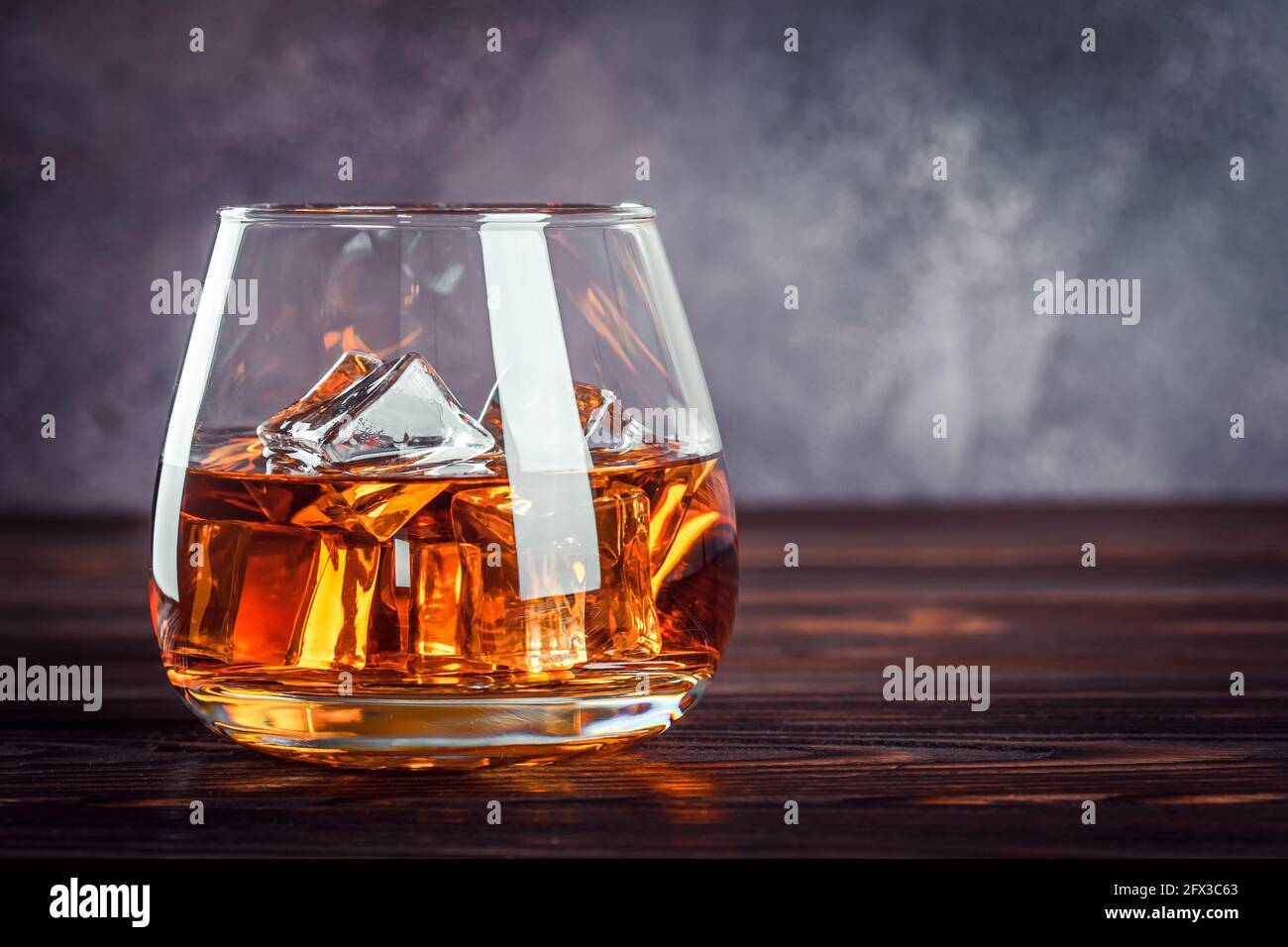 Un bicchiere di whisky sul tavolo di legno marrone scuro. Bevanda alcolica gialla trasparente con ghiaccio. Brandy, bourbon. Bevanda alcolica forte. Spazio di copia f Foto Stock