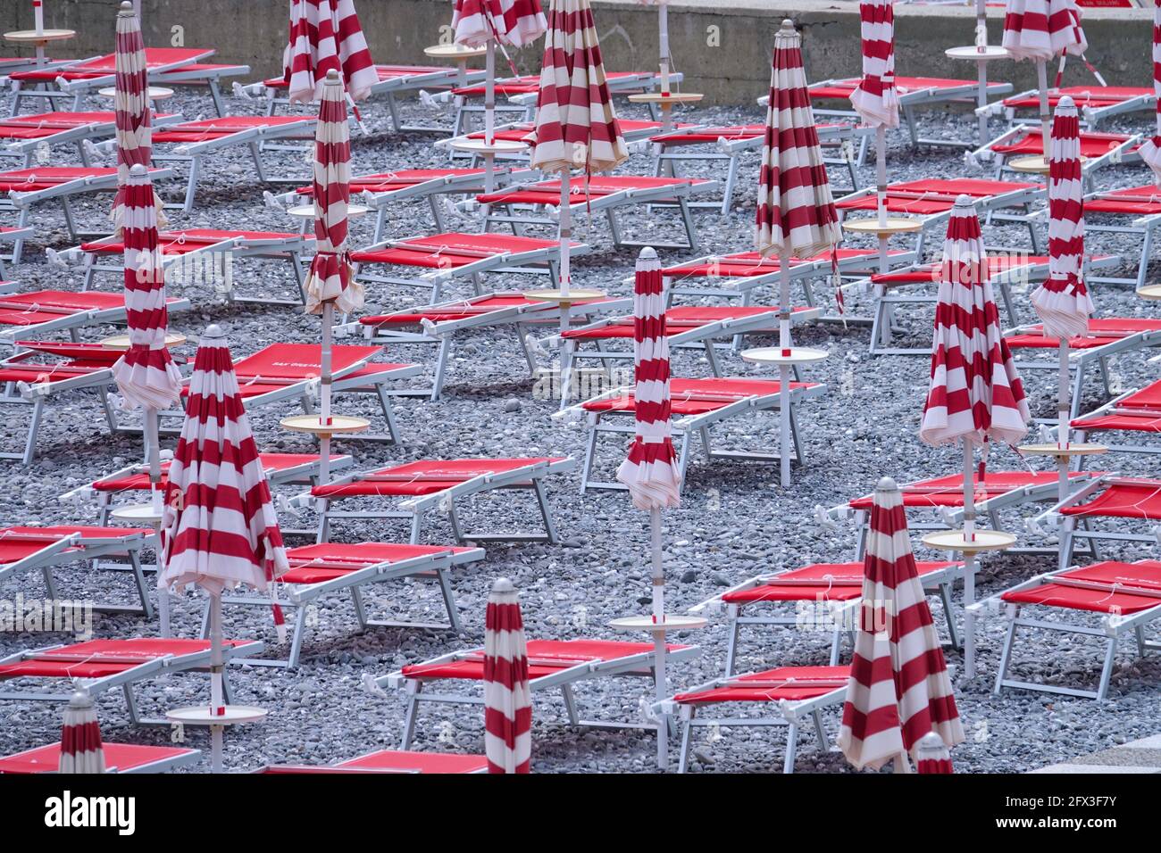 Sedie a sdraio vuote con ombrelloni ripiegati in Italia Foto Stock
