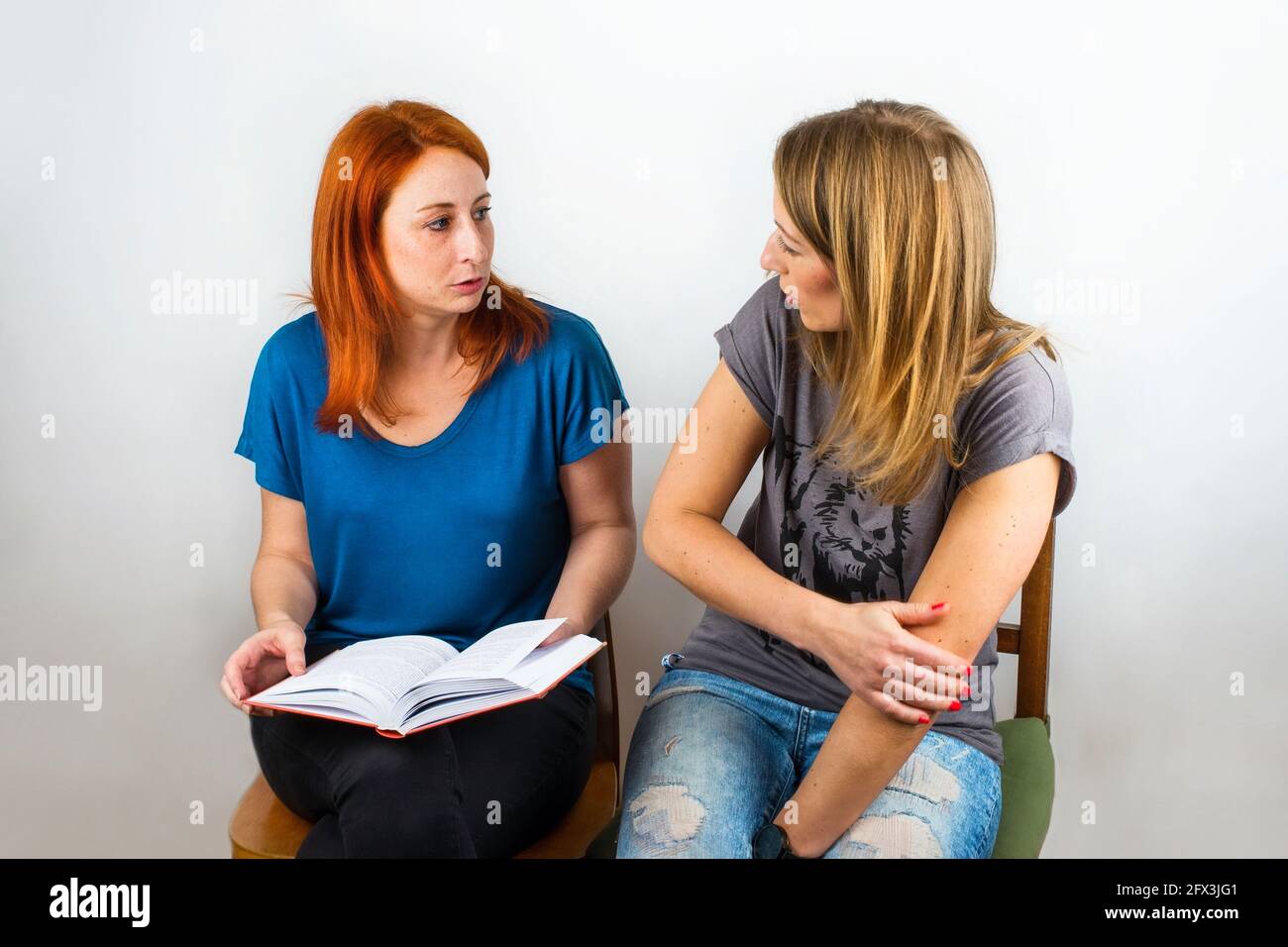 Due giovani donne attraenti siedono sopra il libro e parla del soddisfare. Su sfondo grigio. Foto Stock