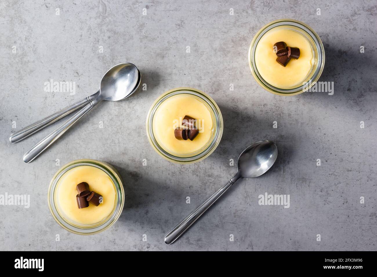 Tre bicchieri di budino di vaniglia disposti verso l'alto linea diagonale sul piano di appoggio grigio Foto Stock