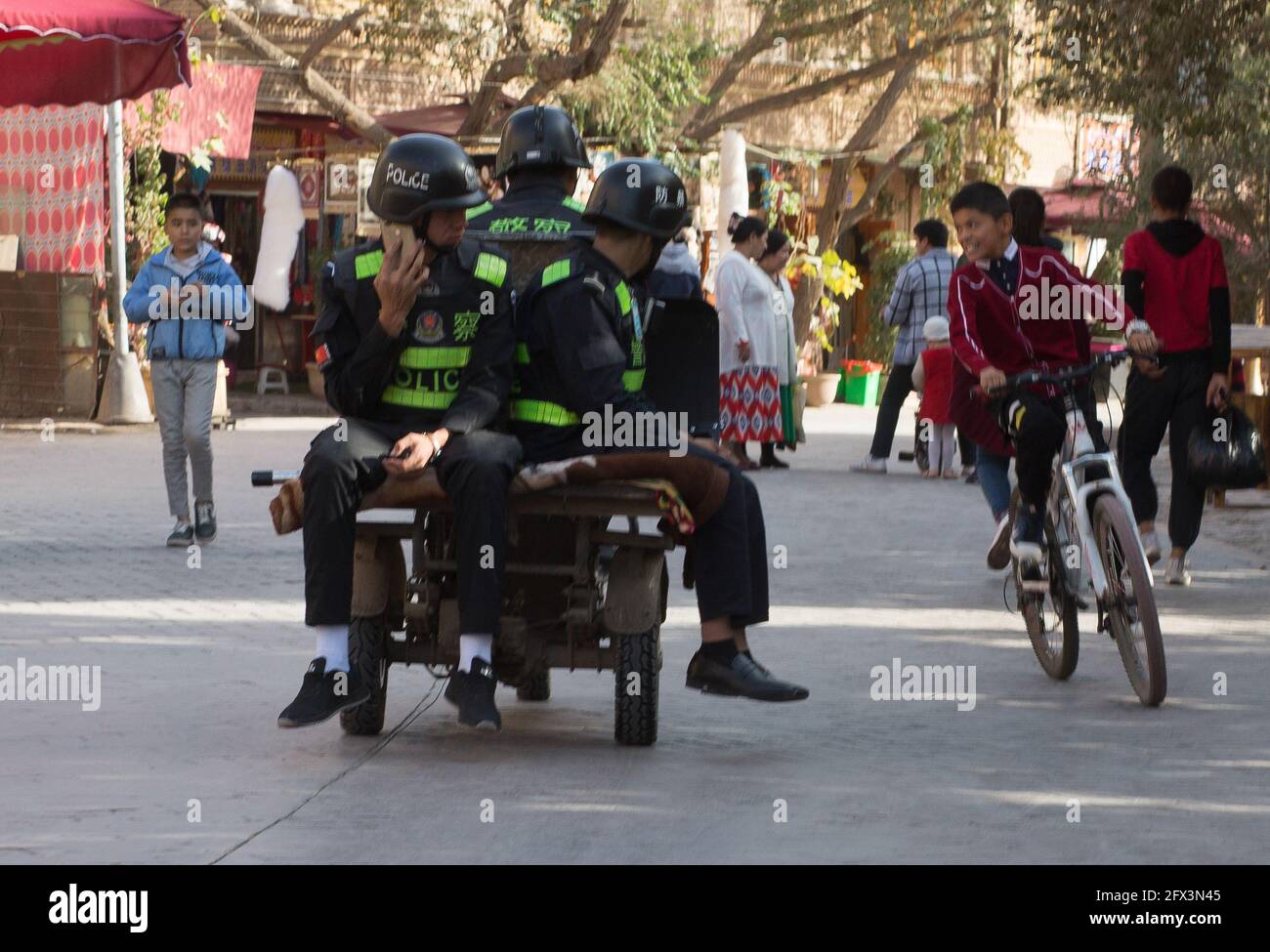 Polizia in un veicolo che guarda su Ordaishki strada mentre un bambino su una bicicletta si avvicina loro. Kashgar, Cina Foto Stock