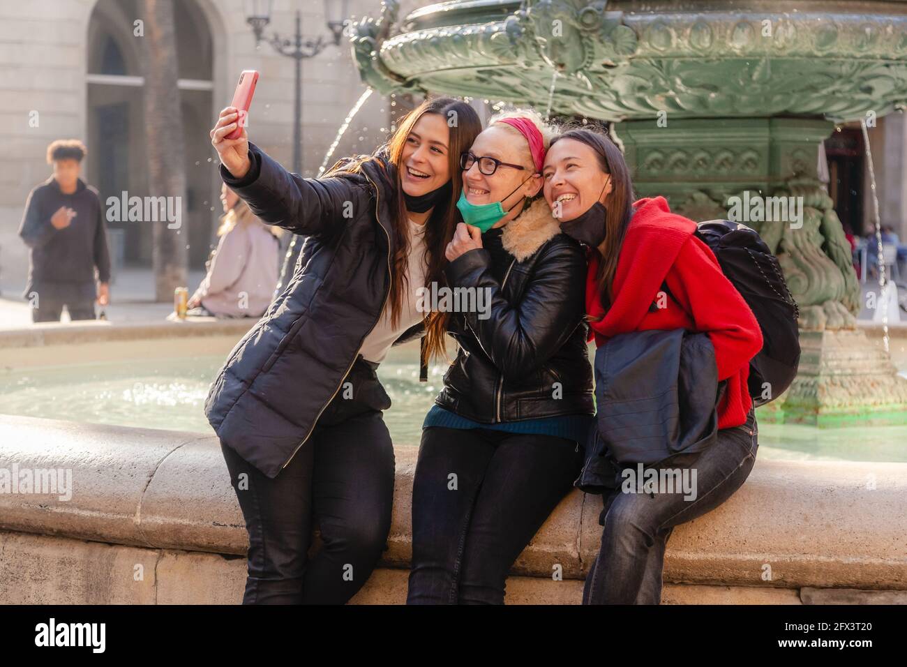 Tre amici donne che catturano un selfie con uno smartphone durante la covid 19 pandemia, indossare maschere di protezione, nel centro di Barcellona Foto Stock