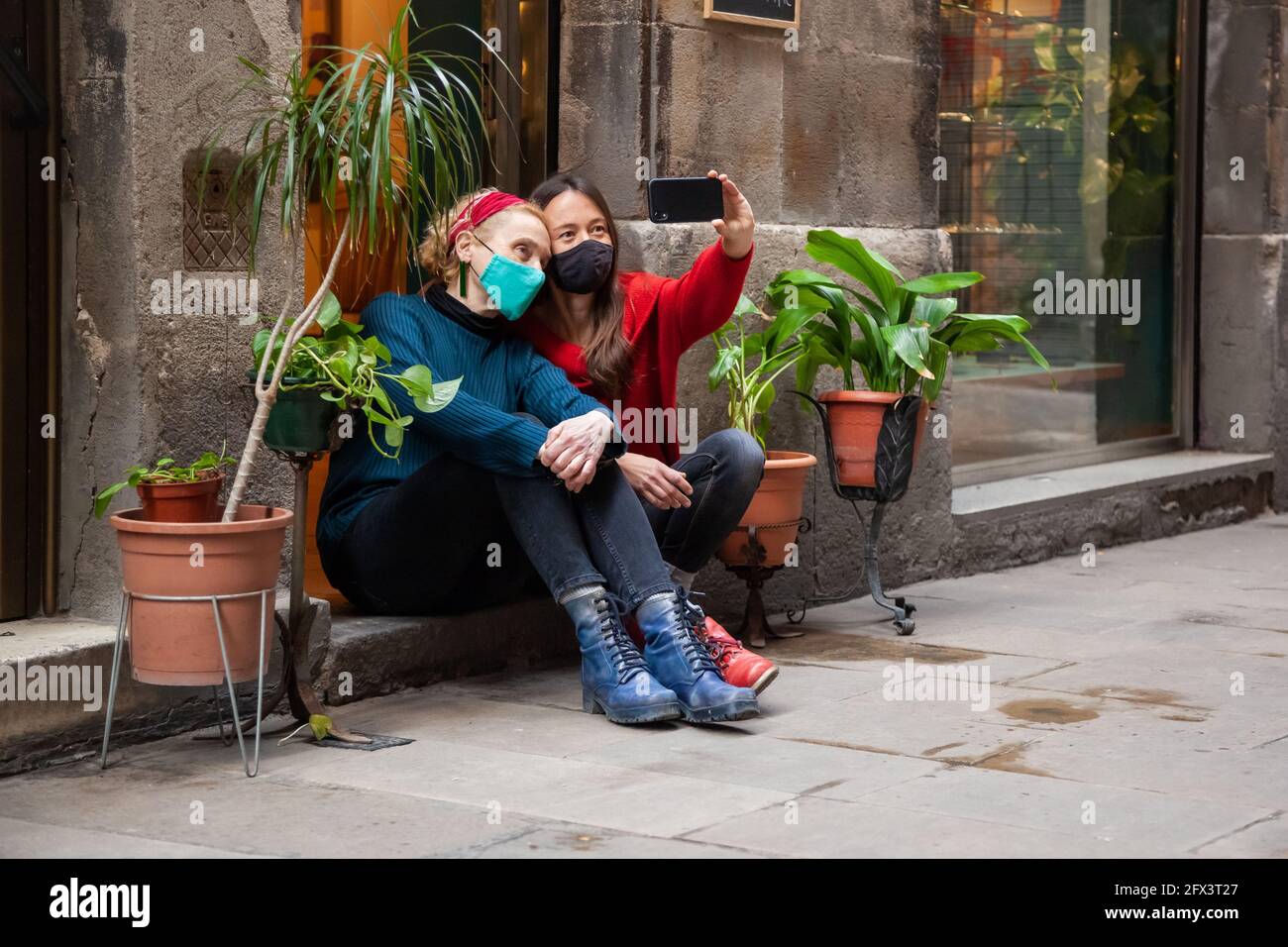 Due amici di donna che indossano maschere di protezione seduta vicino insieme prendendo selfie con smartphone. Concetto: Stile di vita cittadino, covid-19, tutti i giorni noi Foto Stock