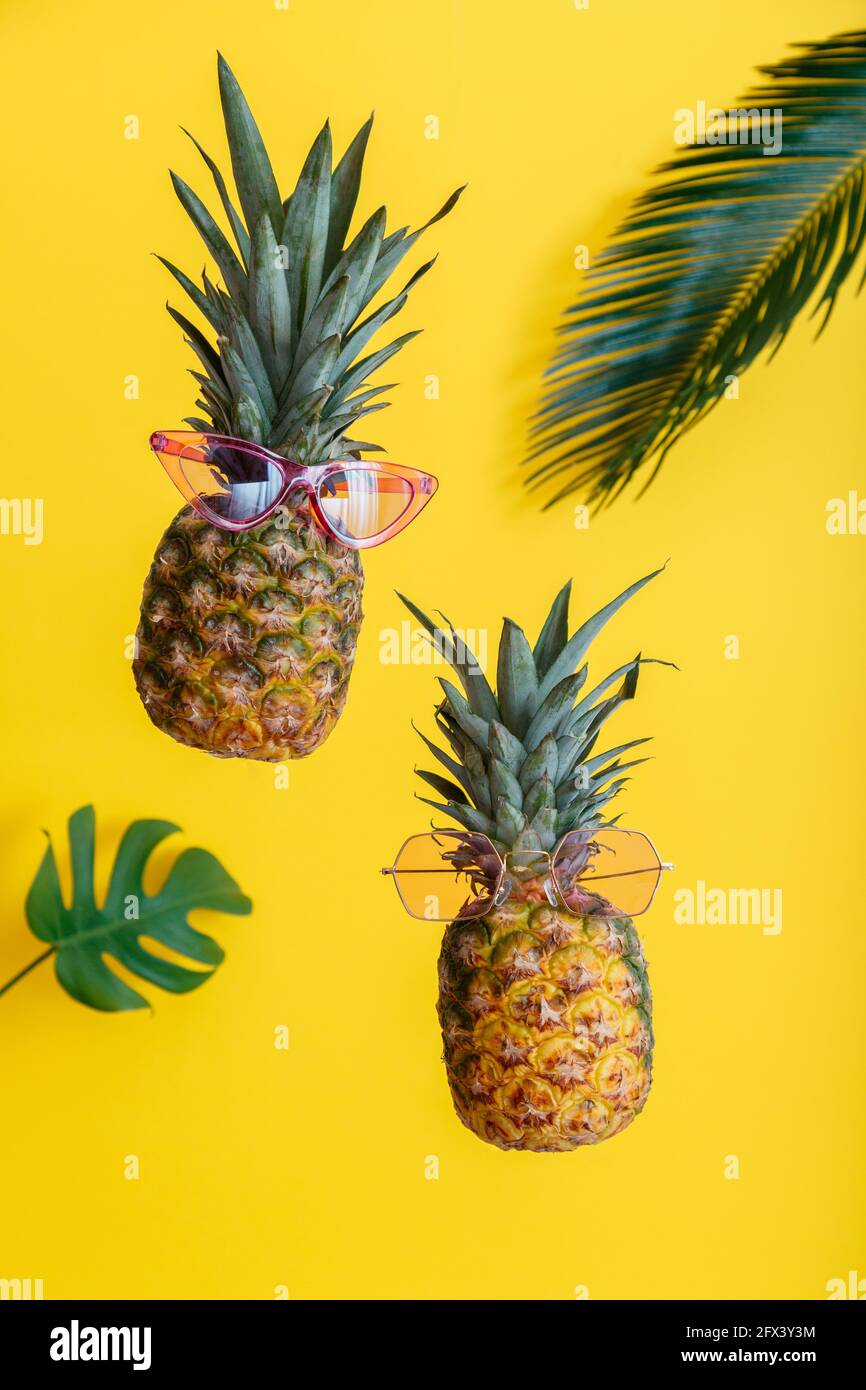 Ananas facce creative in occhiali da sole a colori con foglie di palma su sfondo estivo di colore giallo. Frutti tropicali estivi che levitano ananas. Foto Stock
