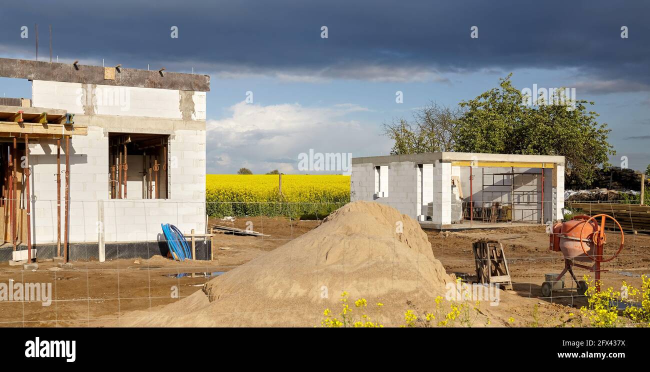 Casa rurale in costruzione con campo di colza e nubi tempestose in background. Foto Stock