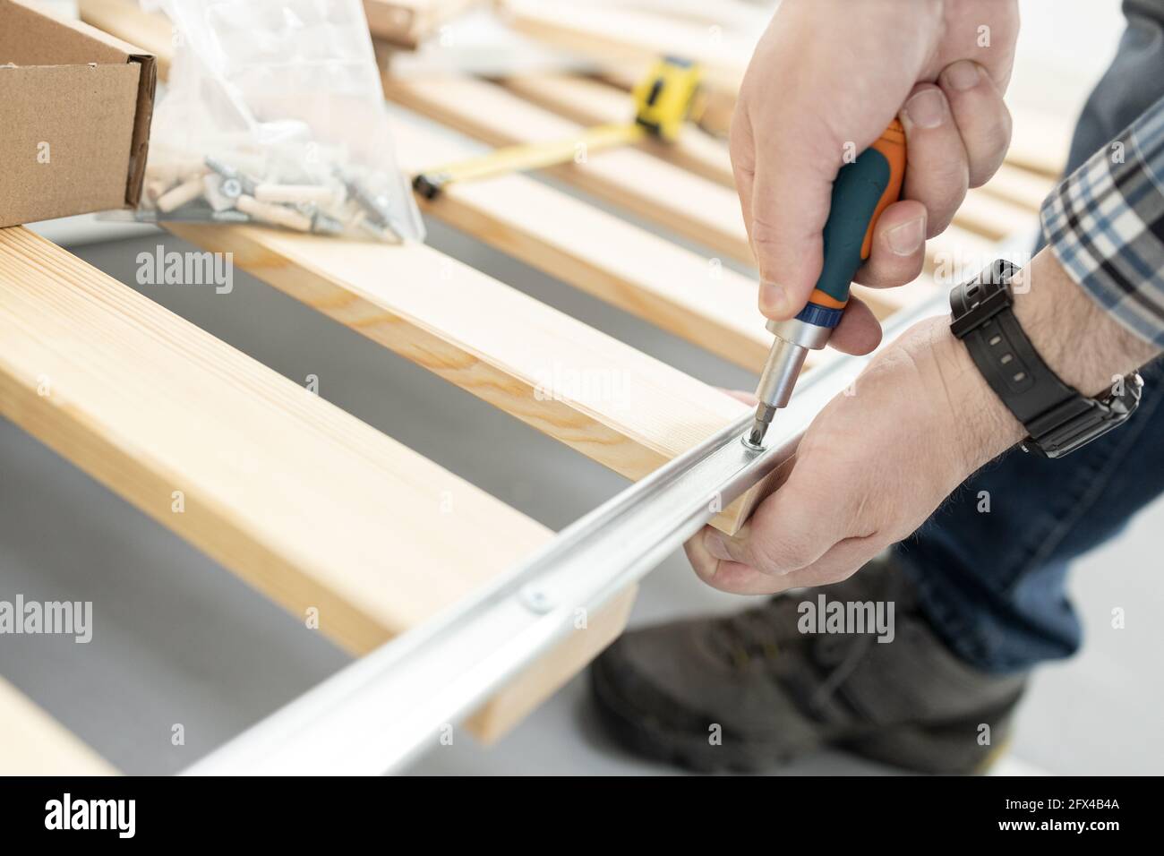 Primo piano di una mano che monta un telaio del letto con un cacciavite. Concetto di montaggio per mobili Foto Stock