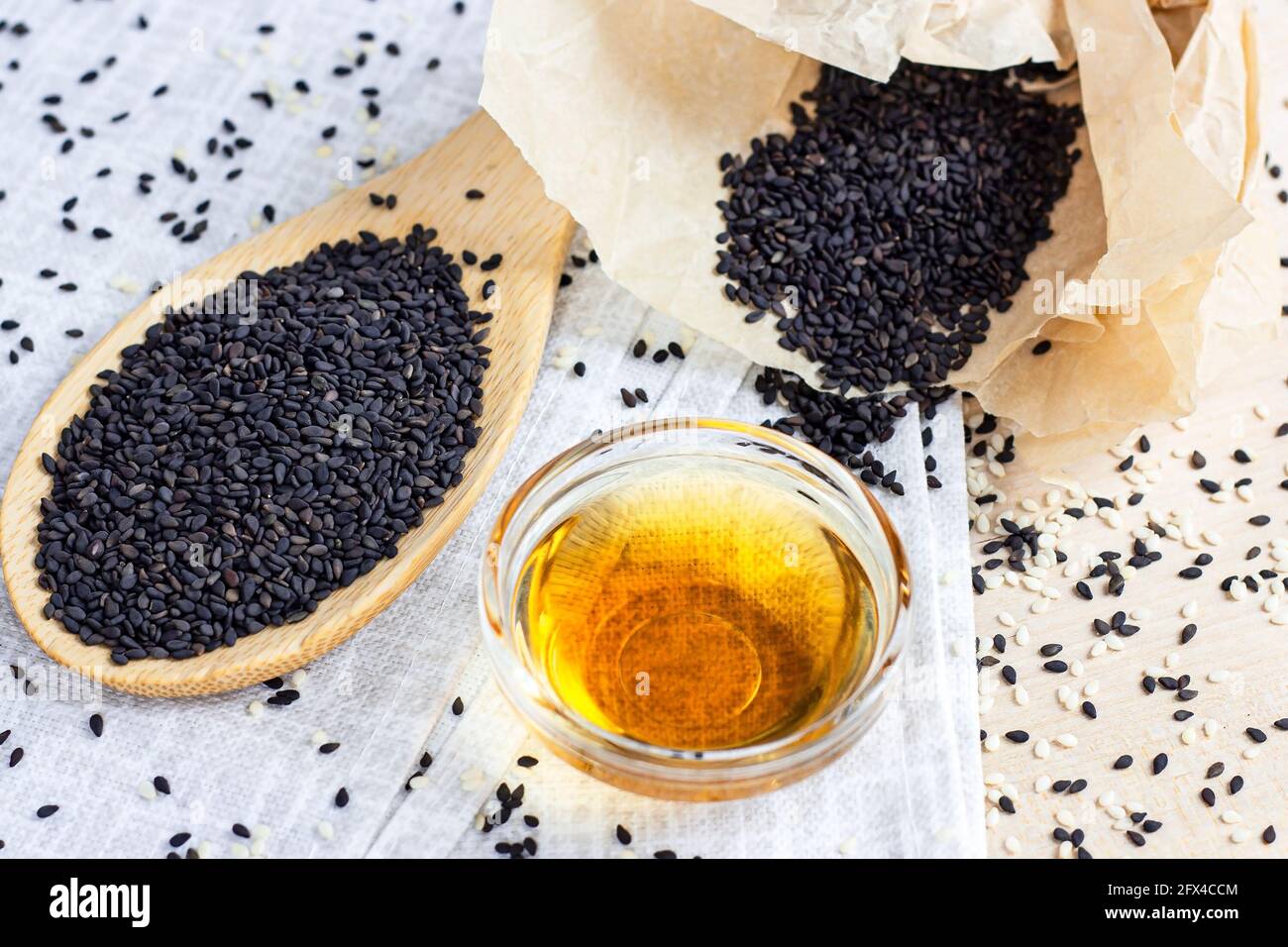 Semi di sesamo nero in un cucchiaio di legno e olio sopra sfondo chiaro in cucina Foto Stock