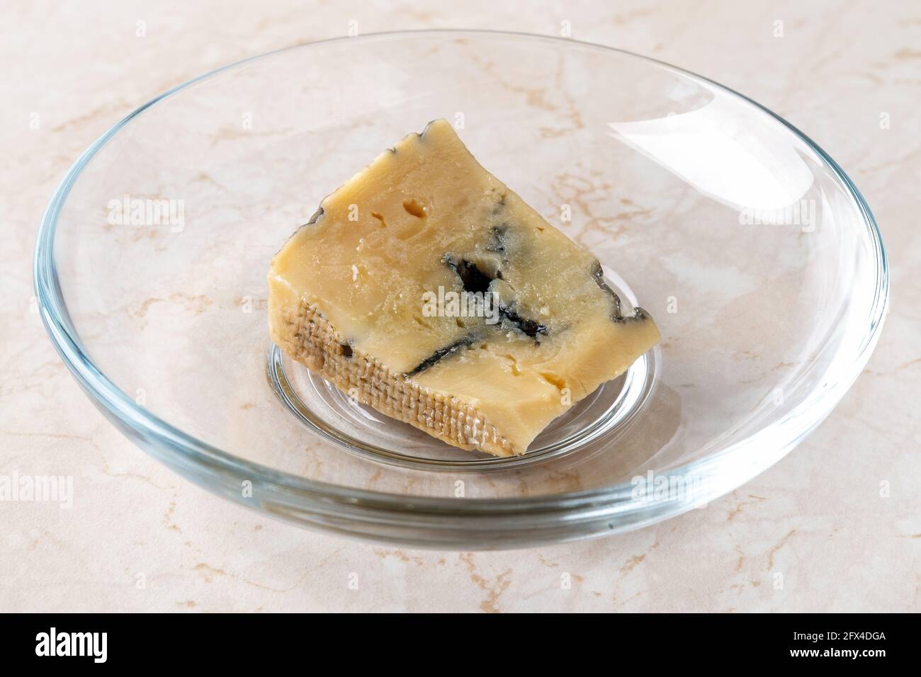 Rottami di formaggio essiccato rovinato. Un piccolo pezzo di formaggio blu dor si è asciugato su un piatto sul tavolo. Cibo viziato a causa di stoccaggio fuori dal frigorifero. Foto Stock