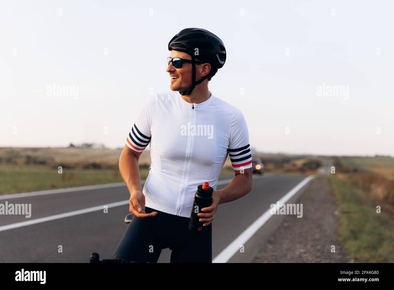 Uomo sorridente in abiti da ciclismo in piedi all'aperto Foto Stock