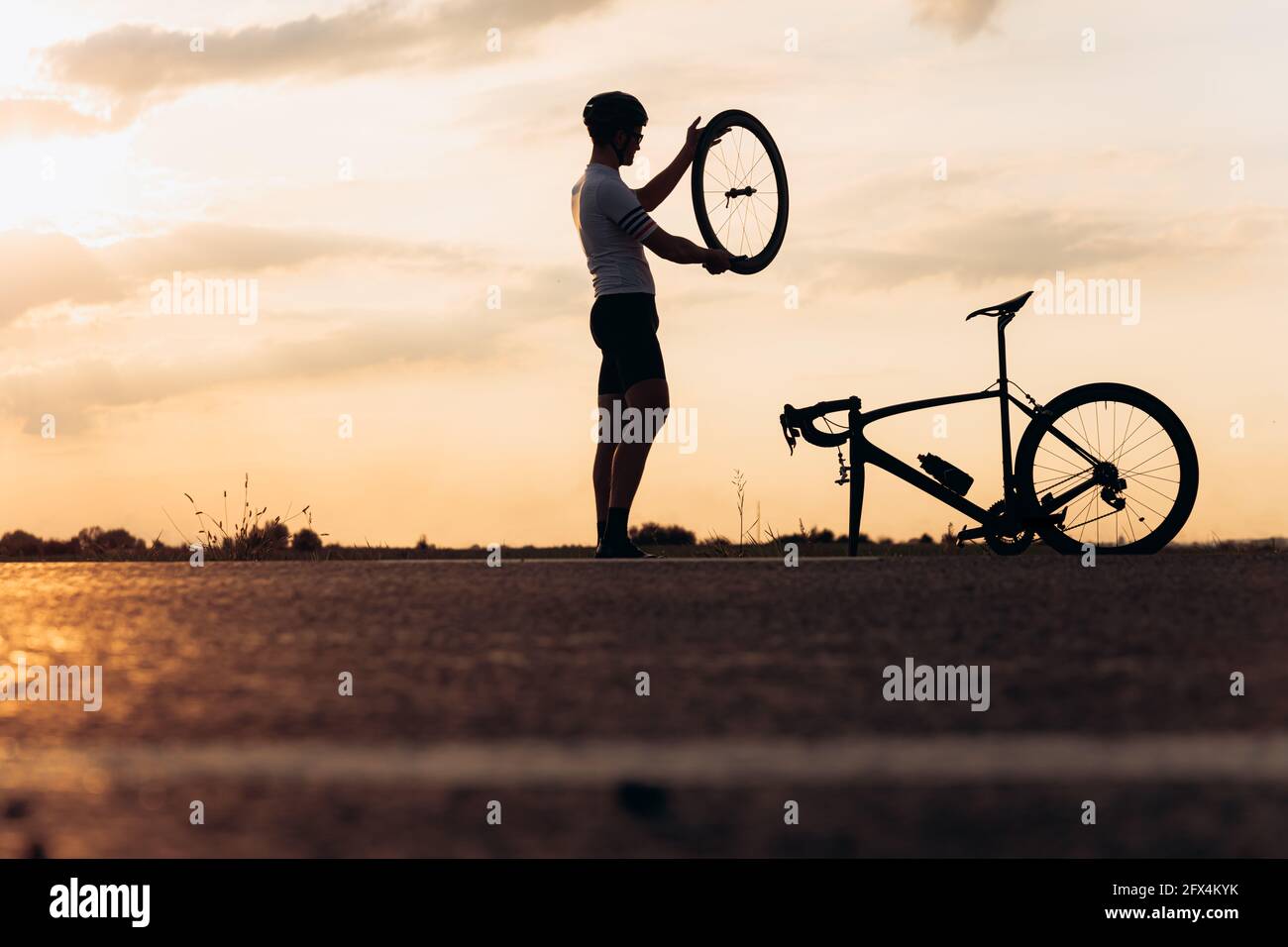 Uomo attivo in silhouette che ripara la moto su strada Foto Stock