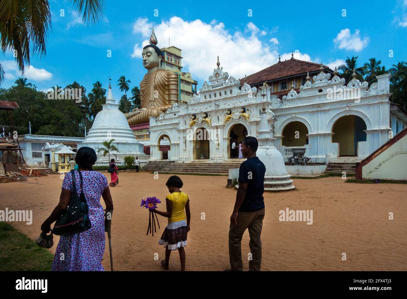 Dikwella, Tempio di Wewurukankala Vihara, Sri Lanka: Una famiglia entra nel cortile del tempio con la statua gigante del Buddha Foto Stock