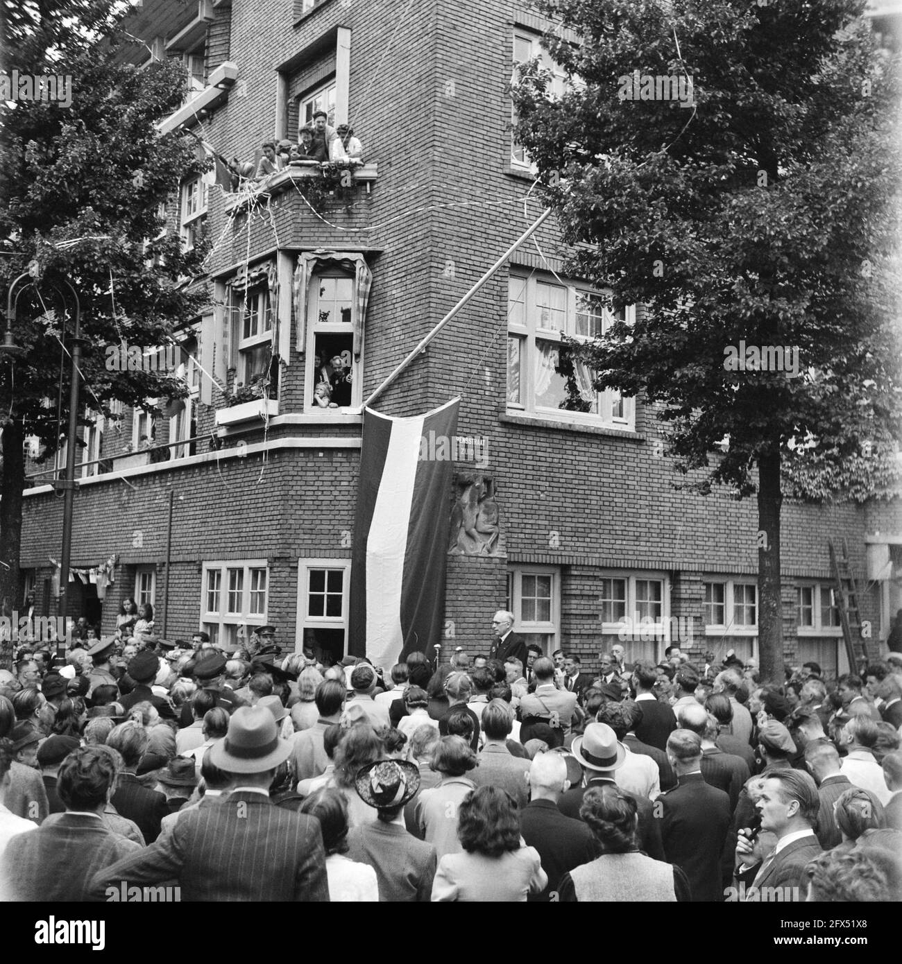 [Incontro festivo all'angolo di Euterpedstraat e Rubensstraat, in occasione del cambio di nome della strada precedente in Gerrit van der Veenstraat. Sulla facciata dell'edificio ad angolo una bandiera olandese copre il nuovo cartello stradale. Il sindaco Feike de Boer ha pronunciato un discorso, 28 giugno 1945, celebrazioni per la liberazione, seconda guerra mondiale, I Paesi Bassi, foto agenzia stampa del XX secolo, notizie da ricordare, documentario, fotografia storica 1945-1990, storie visive, Storia umana del XX secolo, che cattura momenti nel tempo Foto Stock