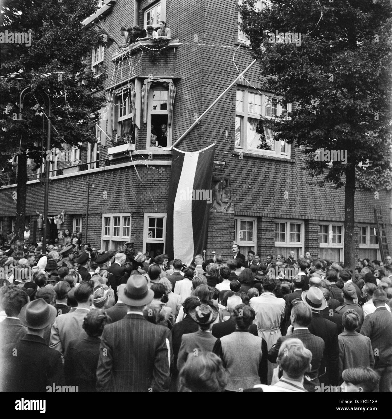 [Incontro festivo all'angolo di Euterpedstraat e Rubensstraat, in occasione del cambio di nome della strada precedente in Gerrit van der Veenstraat. Sulla facciata dell'edificio ad angolo una bandiera olandese copre il nuovo cartello stradale. Vedova di Gerrit van der Veen ha tenuto un discorso], 28 giugno 1945, celebrazioni per la liberazione, seconda guerra mondiale, Paesi Bassi, foto agenzia stampa del xx secolo, notizie da ricordare, documentario, fotografia storica 1945-1990, storie visive, Storia umana del XX secolo, che cattura momenti nel tempo Foto Stock