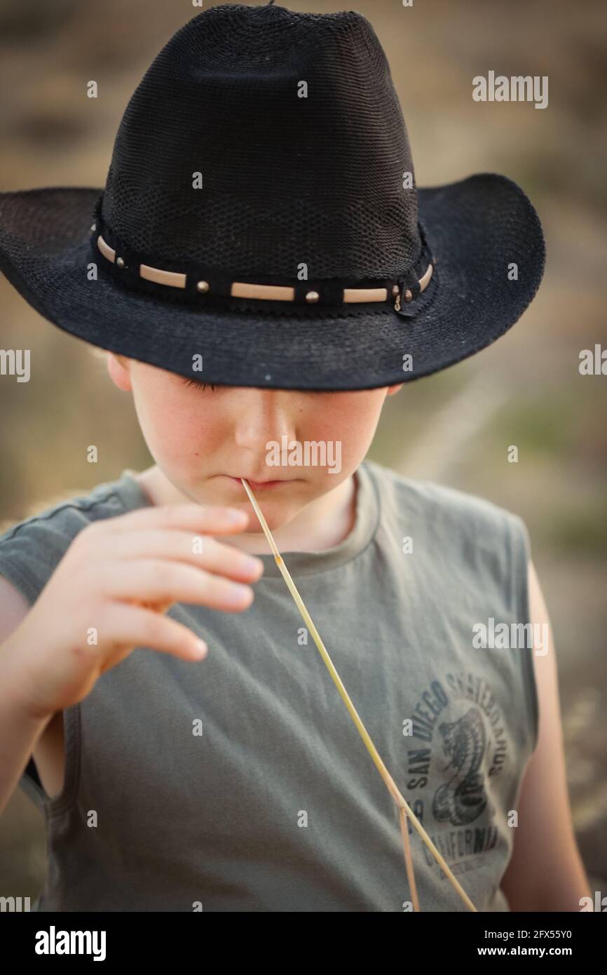 Carino biondo australiano piccolo ragazzo che indossa un cappello nero con  erba in bocca guardando giù Foto stock - Alamy