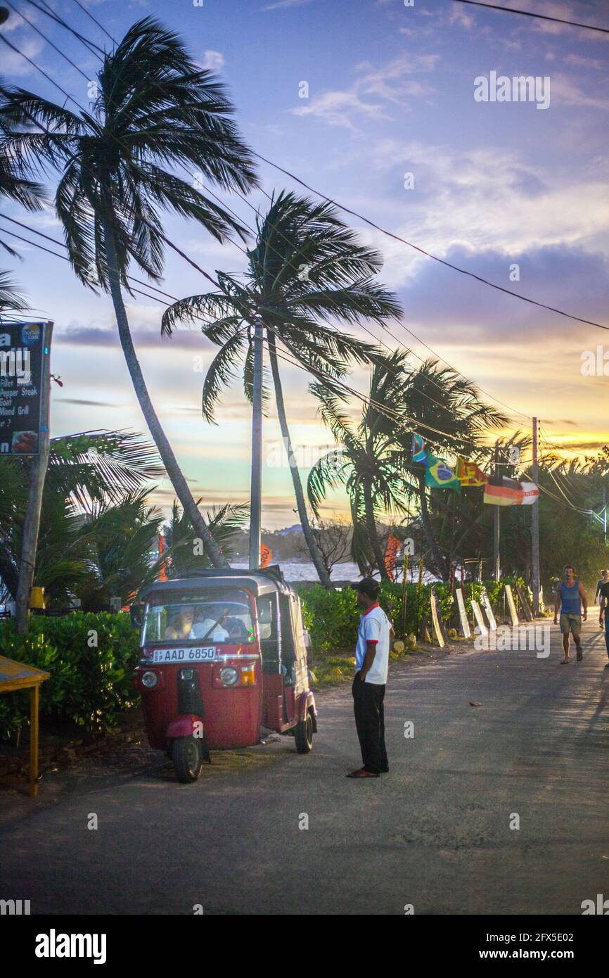 Auto Rickshaw in attesa sul lato della strada con palme e cielo viola al tramonto, Tangalle, Provincia del Sud, Sri Lanka Foto Stock