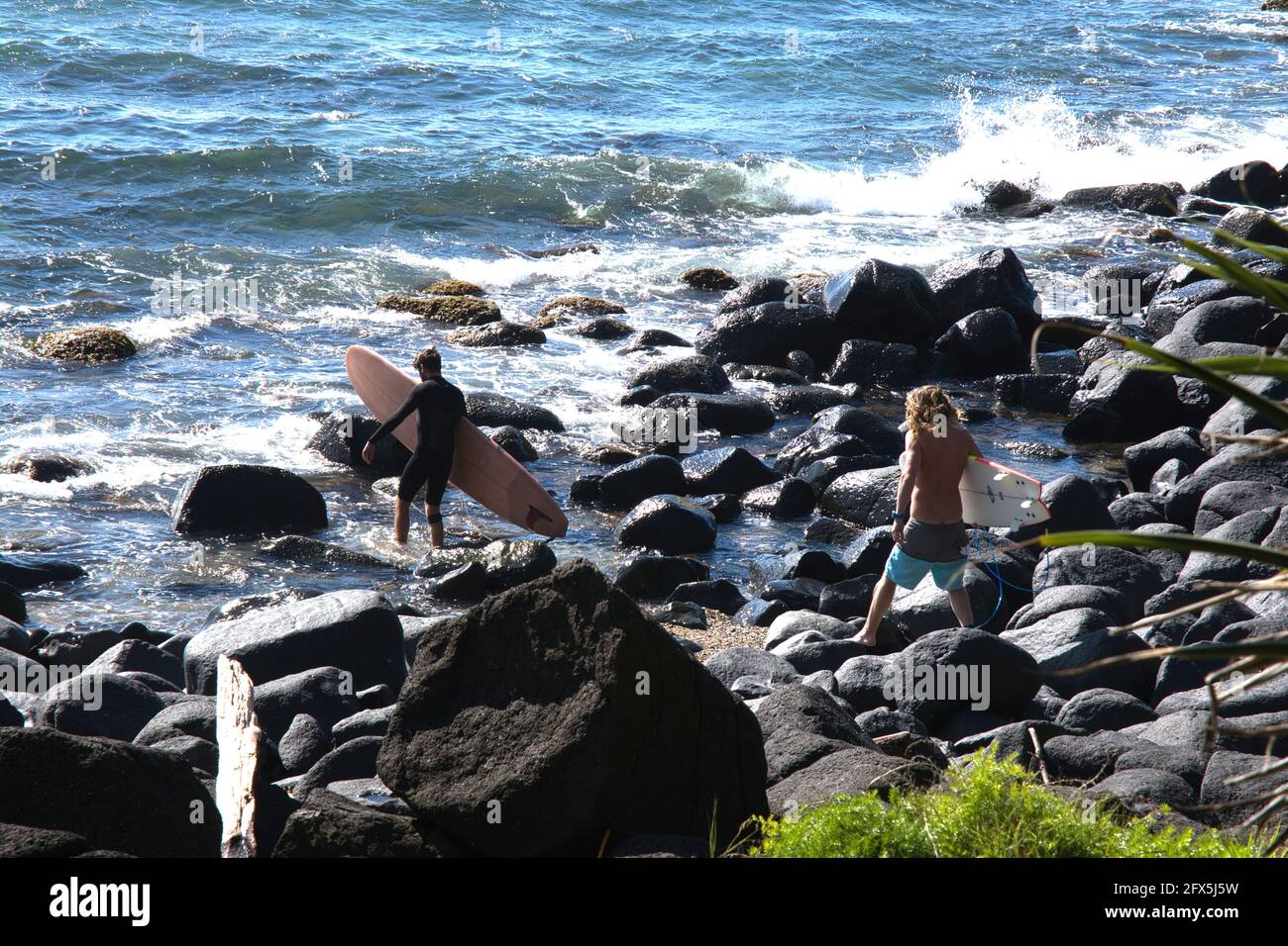 Surfers che arrampicano sopra le rocce per raggiungere il surf a. Burleigh Heads nel Queensland Australia Foto Stock